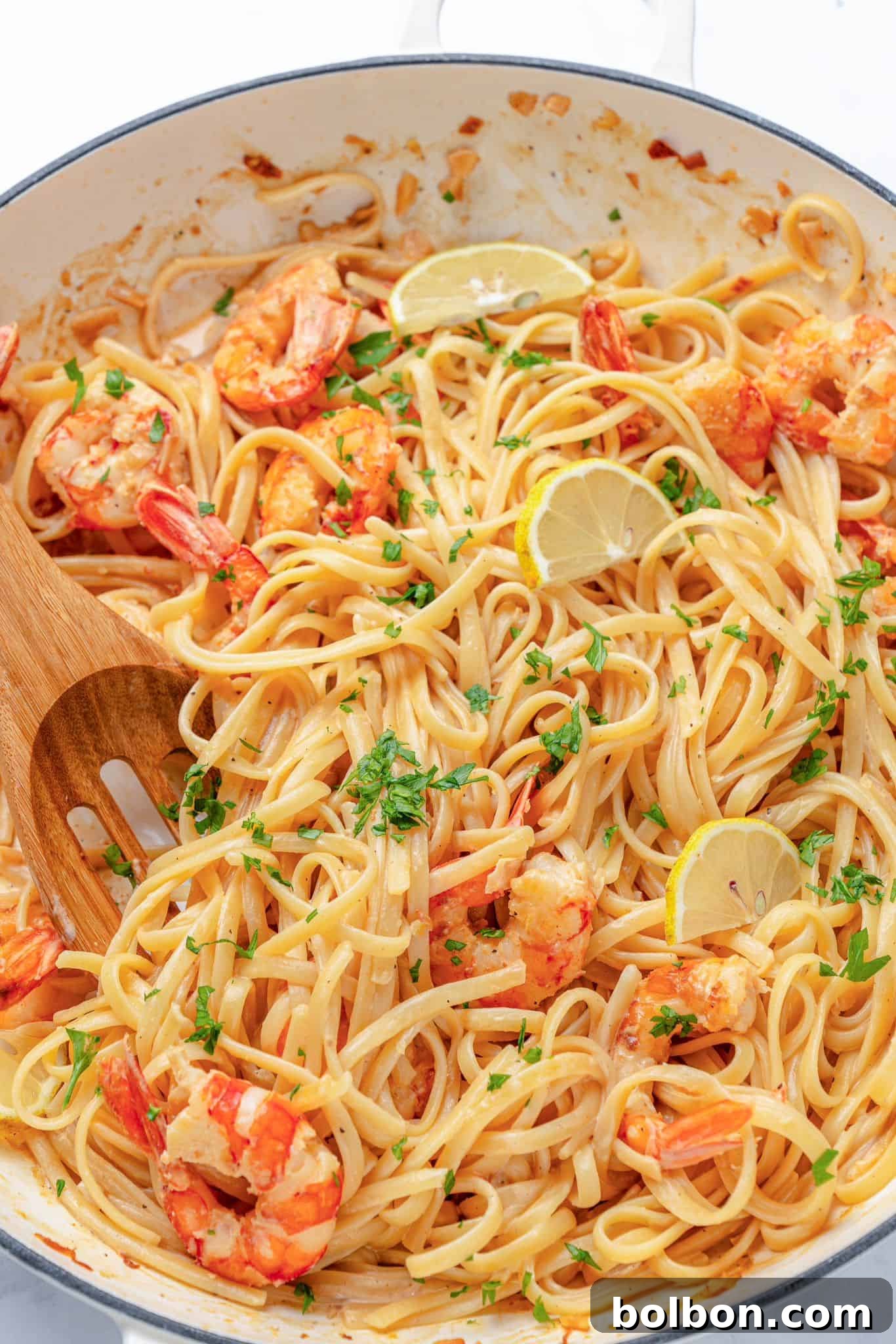 Zesty Lemon Garlic Shrimp Pasta 9 A dish of shrimp linguine is garnished with lemon slices and parsley. The pasta is mixed with succulent shrimp, and a wooden spoon is visible in the creamy sauce.