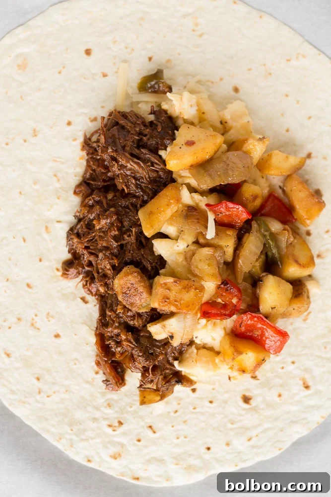 A plate of two freshly made Make-Ahead Beef Breakfast Burritos, garnished with fresh cilantro and a side of salsa.
