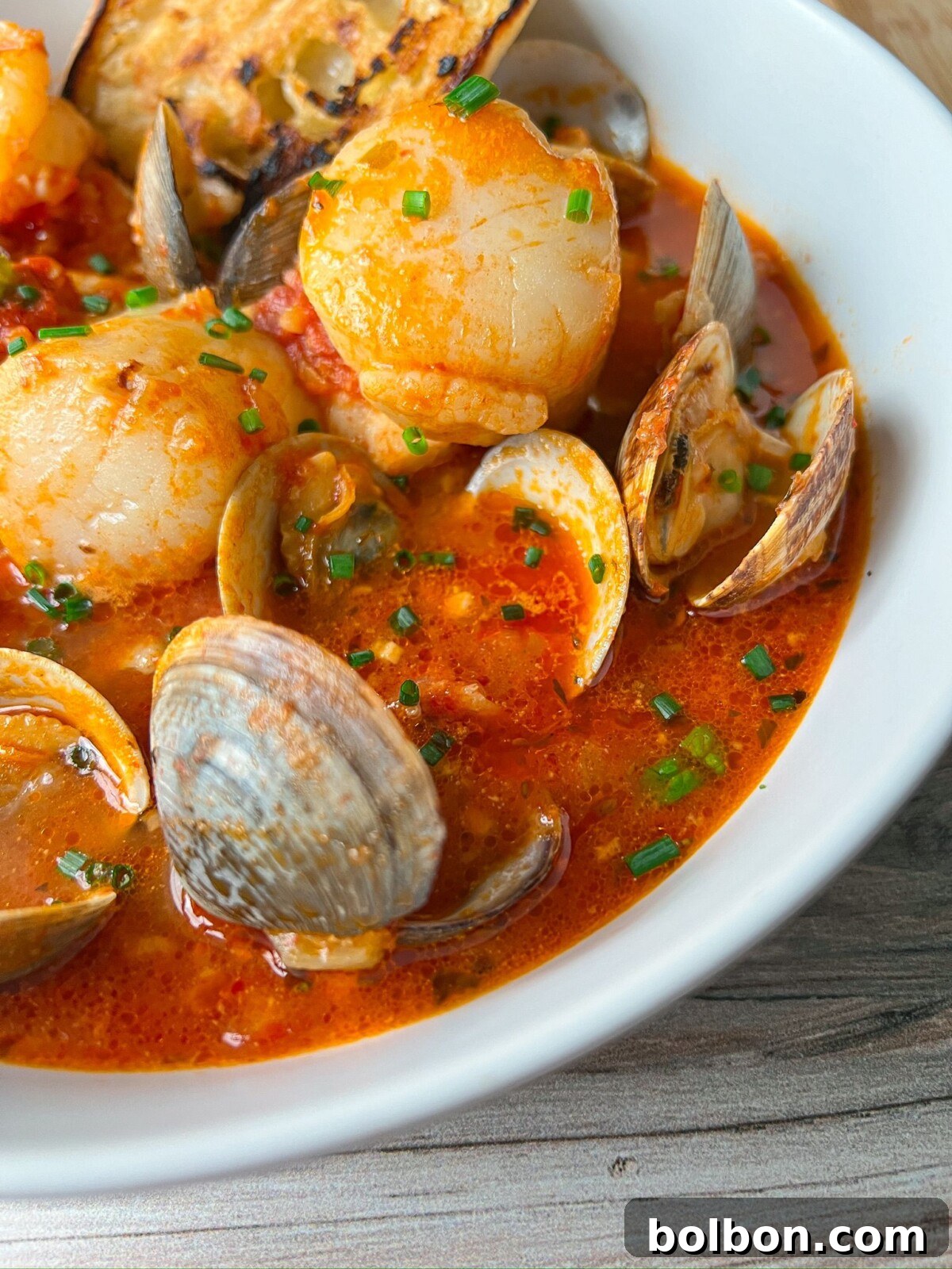 A vibrant bowl of Cioppino seafood stew overflowing with fresh clams, shrimp, and fish in a rich tomato broth, garnished with fresh herbs, and served with crusty bread on the side.