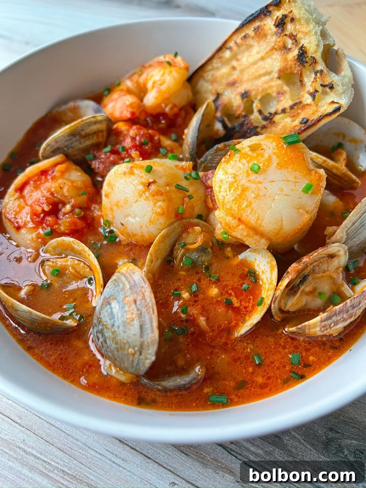 A beautifully presented bowl of Cioppino with a variety of seafood, garnished with fresh parsley and a slice of lemon, next to a glass of white wine.