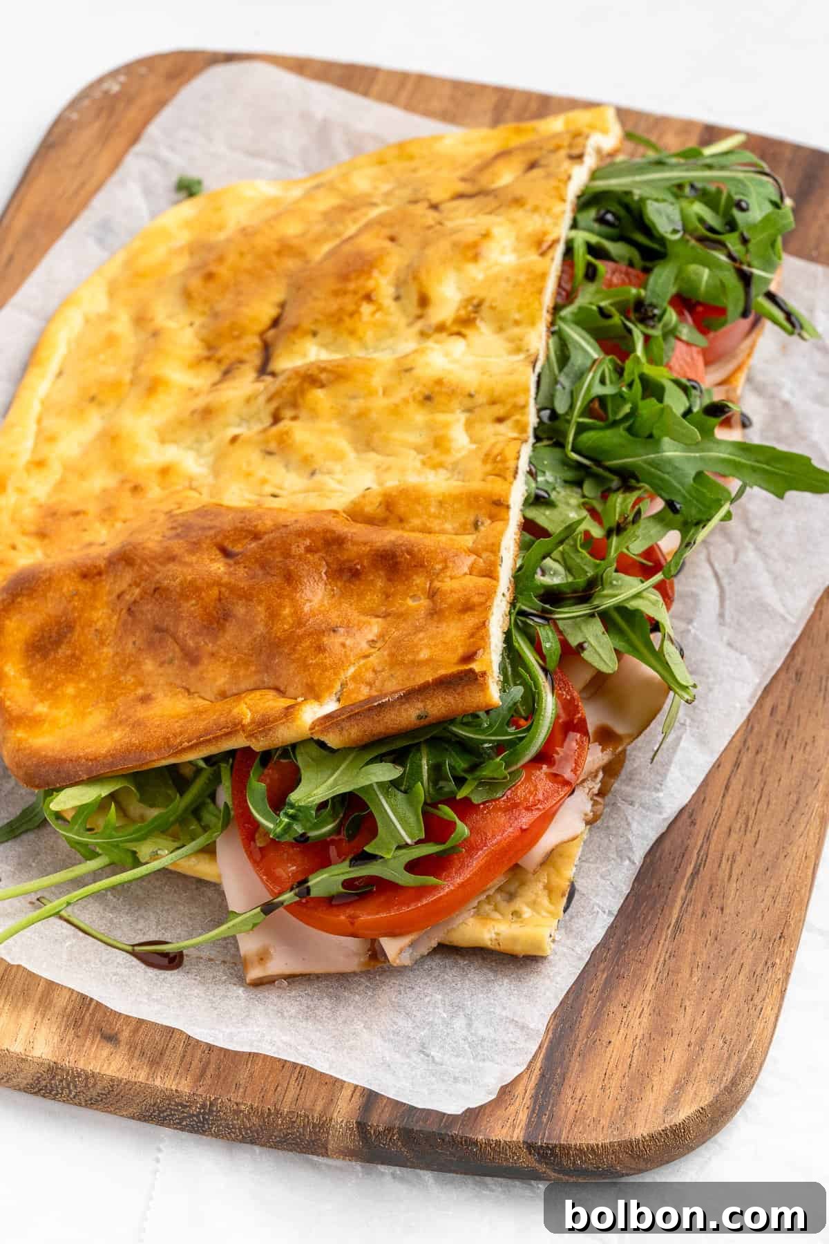 Protein-Packed Cottage Cheese Flatbread 8 A folded flatbread sandwich on a wooden board, filled with sliced turkey, fresh tomato, arugula, and cheese. The bread appears golden and lightly toasted, resting on a piece of parchment paper.