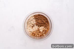 A glass bowl containing oats, cocoa powder, and other dry baking ingredients on a white marble surface, viewed from above.