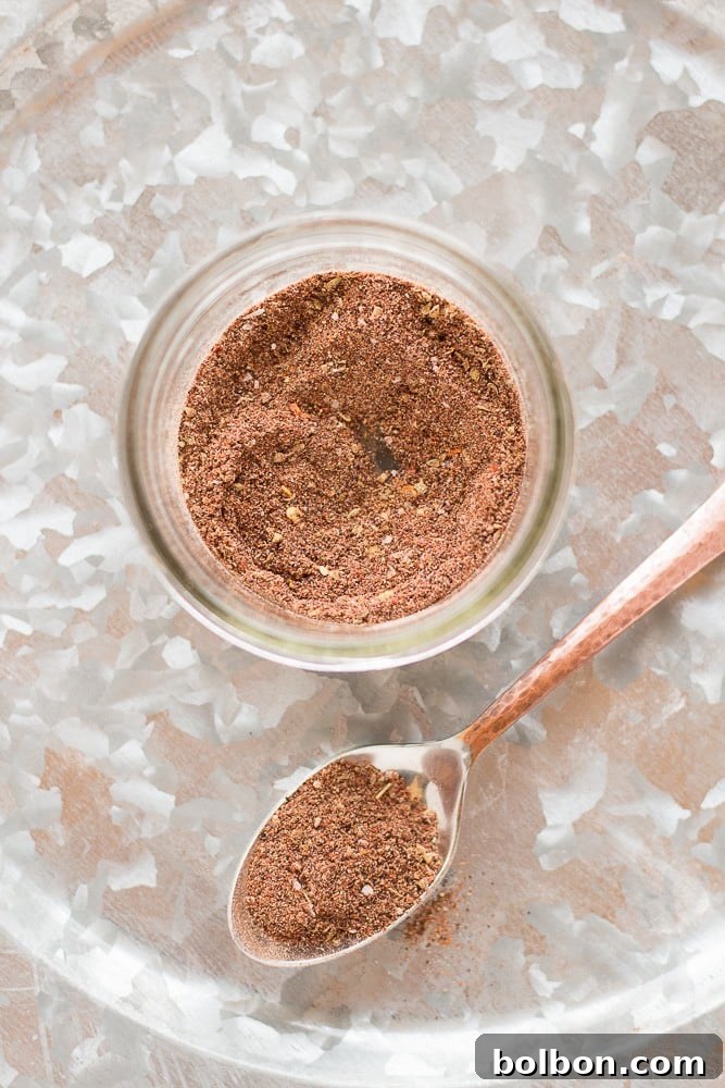 Two glass jars filled with homemade taco seasoning, labeled and ready for storage on a rustic wooden surface, with loose spices in the foreground.