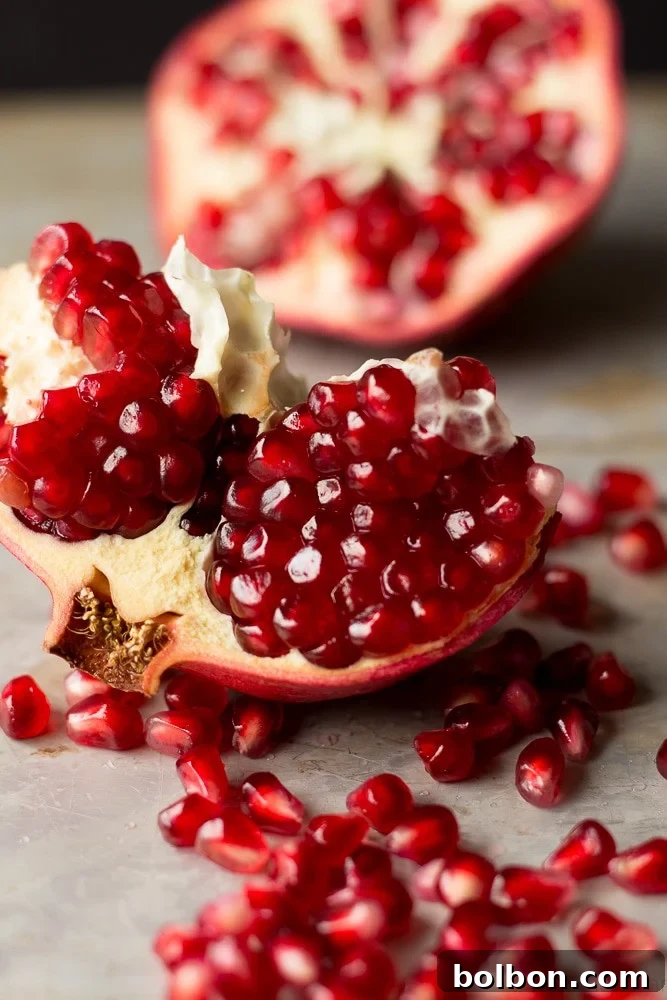 Hand holding a halved pomegranate over a bowl, illustrating a method for de-seeding.