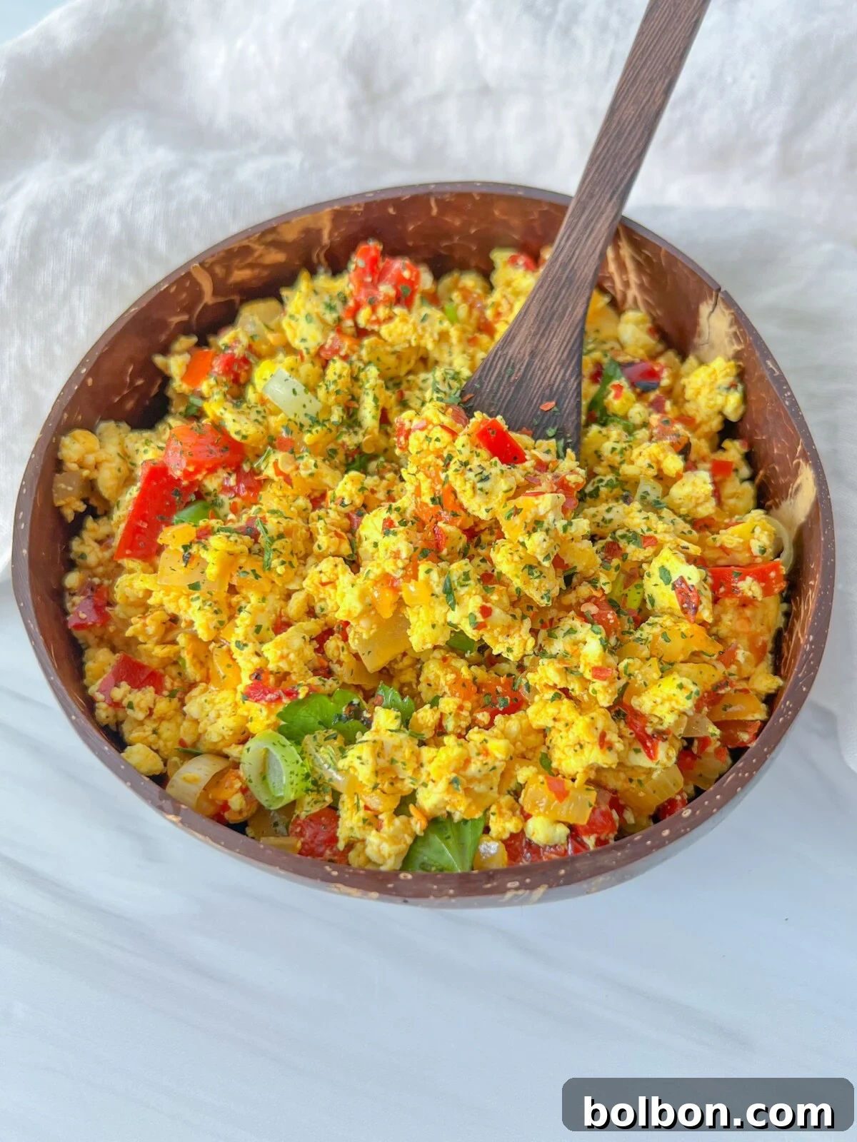 Golden tofu scramble with onions and roasted bell peppers in a skillet, turmeric hue.