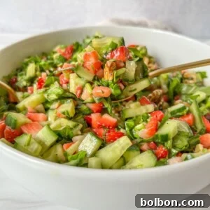 A white bowl filled with Strawberry Spinach Salad made of chopped cucumbers, strawberries, leafy greens, and walnuts, with a fork resting inside.