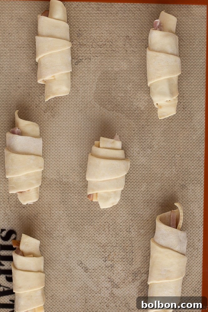 A close-up shot of the raw ham and cheese croissants, neatly rolled and brushed with egg wash, before baking.