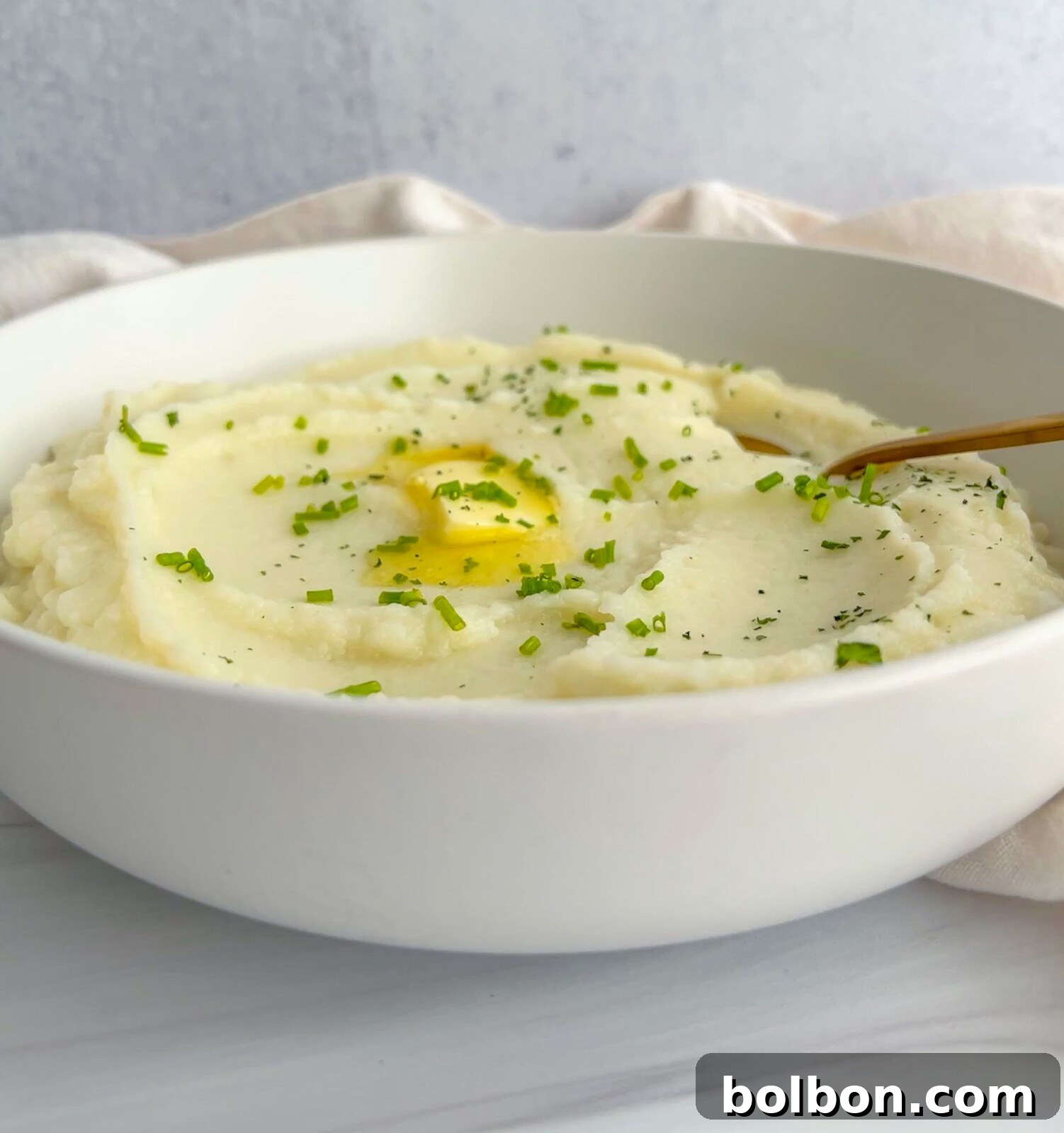 A beautifully plated bowl of creamy cauliflower mash, garnished with fresh herbs and a pat of melted butter.