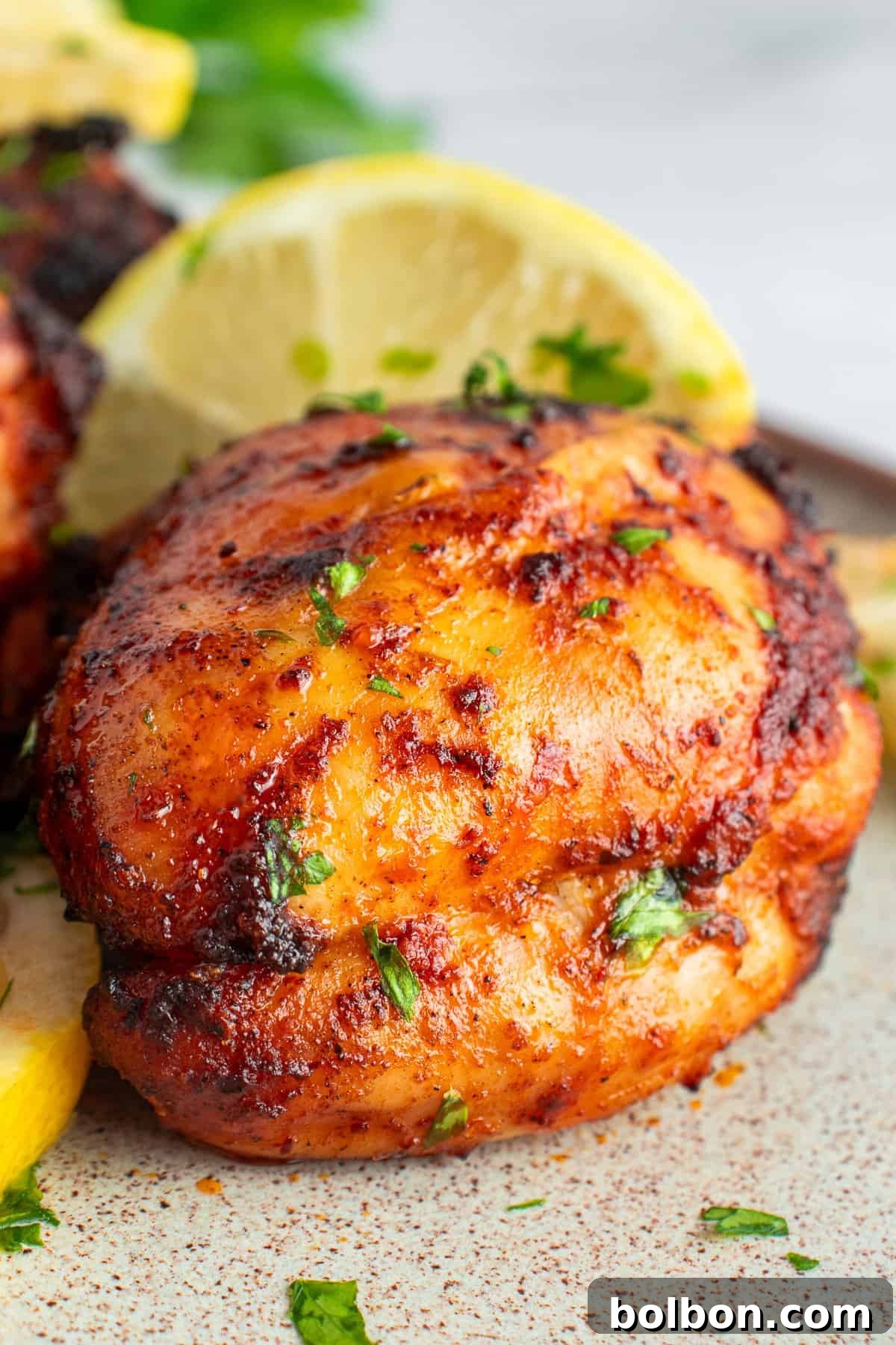 Perfectly Crispy Air Fryer Chicken Thighs 2 Grilled chicken thigh seasoned with spices and garnished with chopped herbs, placed next to a slice of lemon on a plate. The chicken has a crispy, golden-brown exterior.