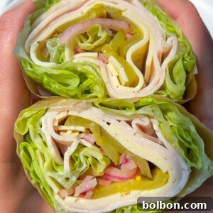 Two hands hold a lettuce wrap sliced in half, revealing layers of turkey, cheese, pickles, onions, and more crisp lettuce rolled tightly inside—no bread in sight for this fresh Lettuce Wrap delight.