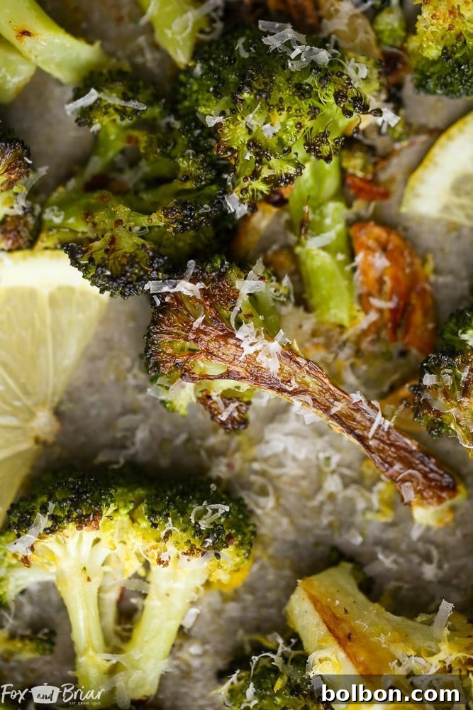 A close-up shot of perfectly roasted lemon parmesan broccoli on a baking sheet with sliced garlic