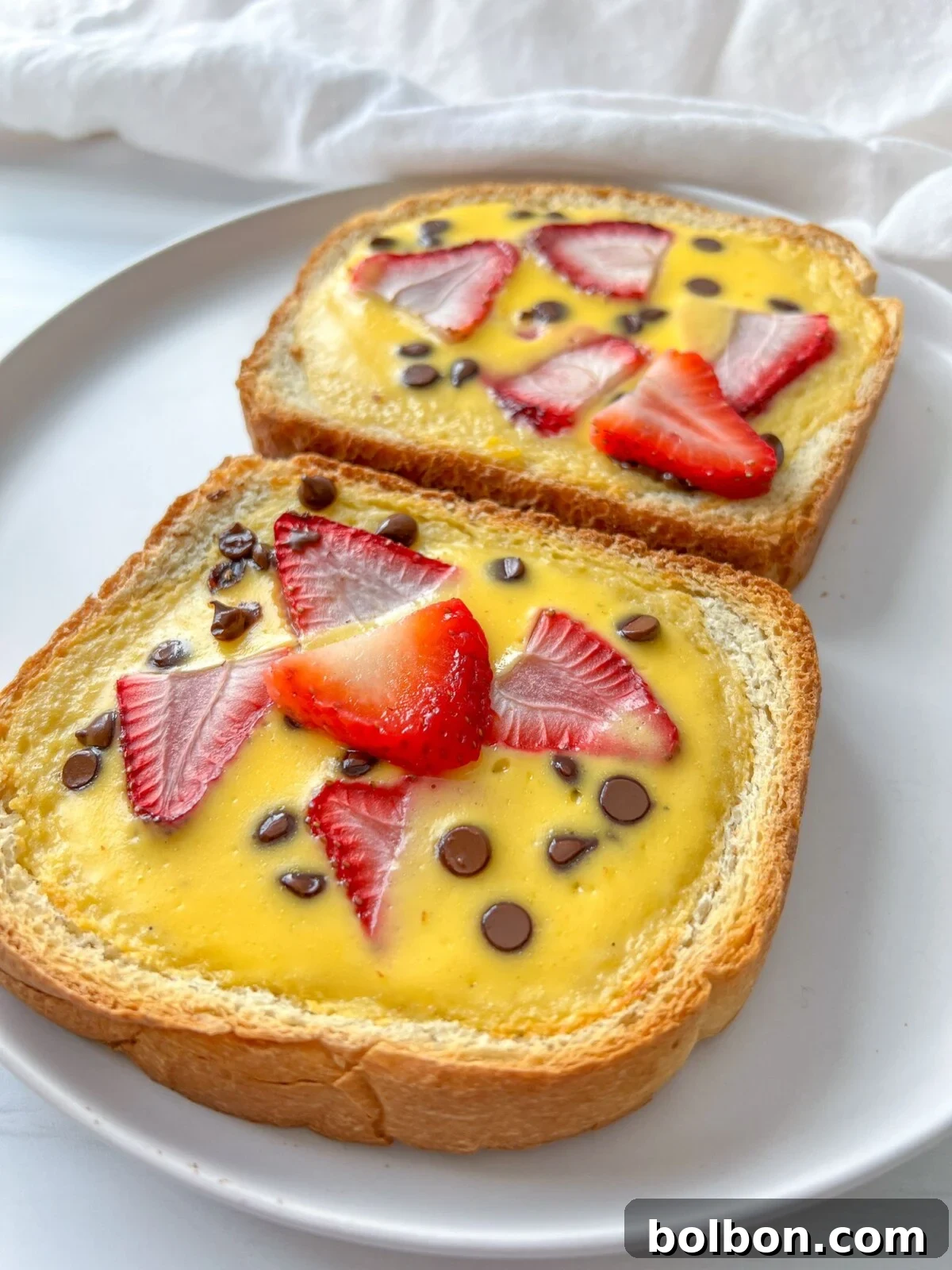 Freshly baked Custard Yogurt Toast with vibrant berries and chocolate chips on a white plate, ready to be enjoyed for breakfast.