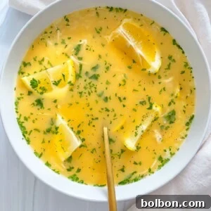 A bowl of creamy Greek Lemon Soup, garnished with fresh herbs and lemon wedges, on a white surface with a golden spoon.
