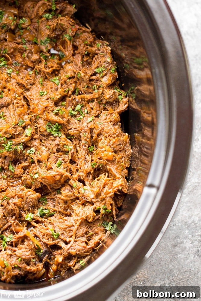 A close-up of the Slow Cooker Mexican Shredded Beef after cooking, showing how easily it shreds with two forks, ready for serving.