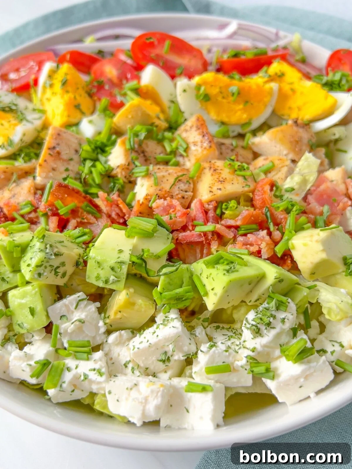 Homemade Cobb Salad Perfection 2 A beautifully arranged Cobb Salad featuring grilled chicken, avocado, cherry tomatoes, hard-boiled eggs, crispy bacon, red onion, fresh romaine lettuce, crumbled feta cheese, all drizzled with a tangy homemade dressing.