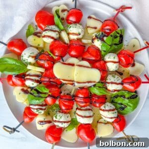 A plate of Valentines Appetizer caprese skewers with cherry tomatoes, mozzarella balls, basil leaves, and heart-shaped cheese slices, drizzled with balsamic glaze, arranged beautifully on a white dish.