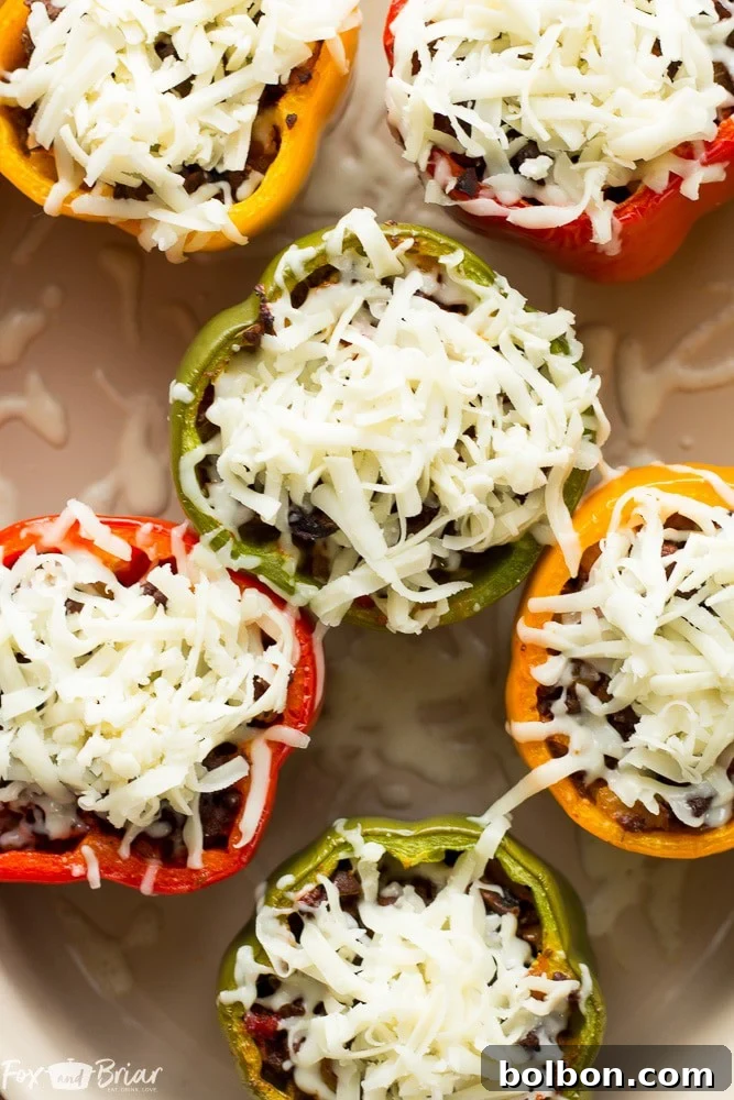 A tray of vibrant bell peppers in red, green, and yellow, hollowed out and ready to be stuffed with the savory pizza filling.