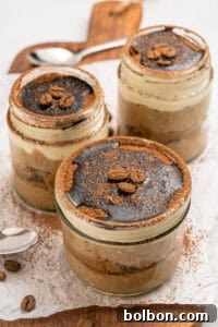 Three glass jars filled with layered tiramisu dessert, topped with cocoa powder, chocolate, and coffee beans, are arranged on a wooden board with a spoon and scattered coffee beans nearby.