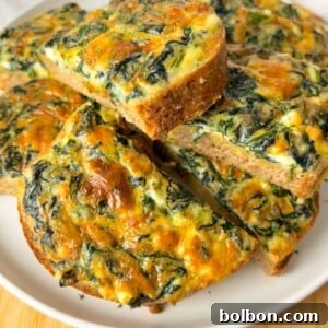 Slices of baked spinach and cheese frittata are arranged on a white plate, showing a golden-brown crust and a colorful mixture of spinach and melted cheese inside.
