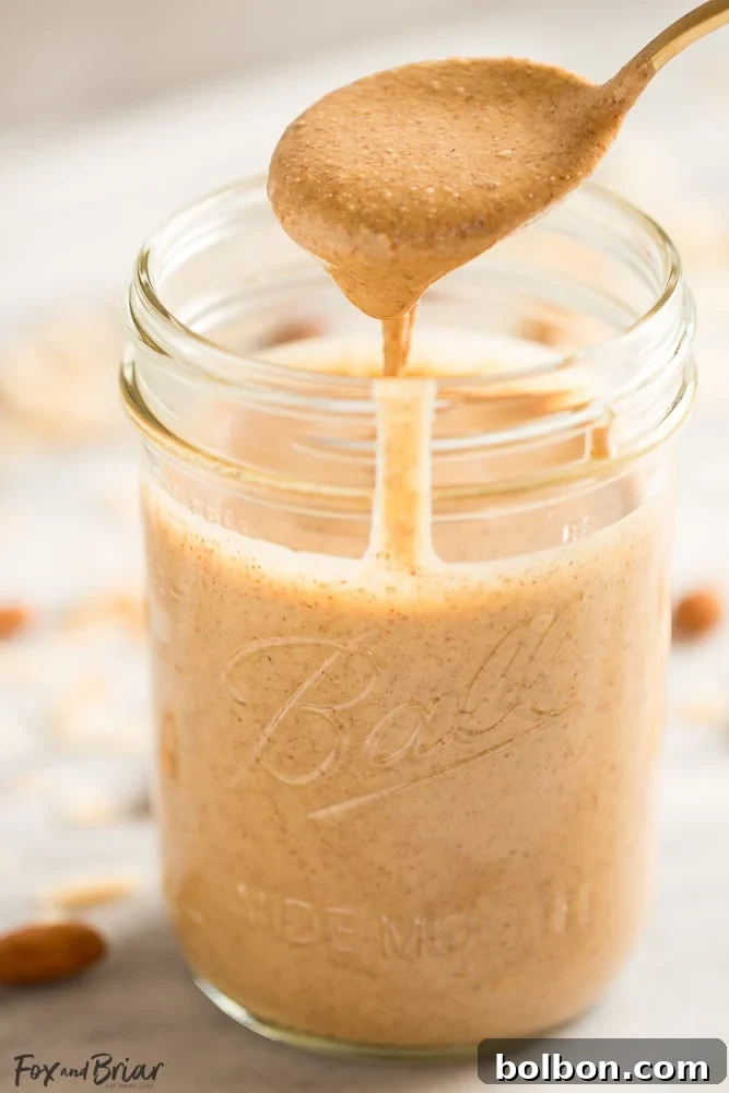 A jar of homemade Toasted Coconut Almond Butter with a spoon, highlighting its texture and deliciousness.