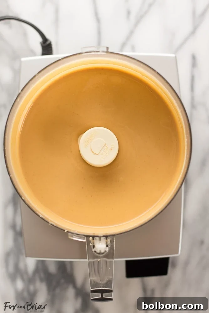 Creamy homemade peanut butter being scooped from a food processor