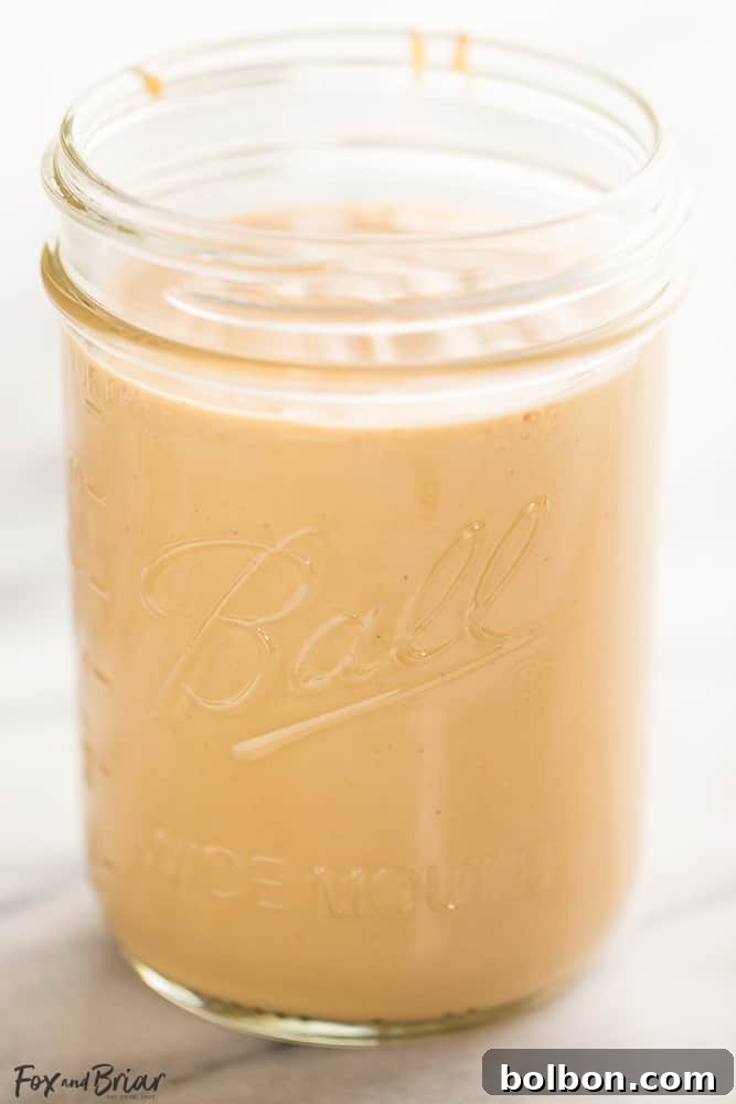 Jar of homemade peanut butter with a spoon, next to whole peanuts