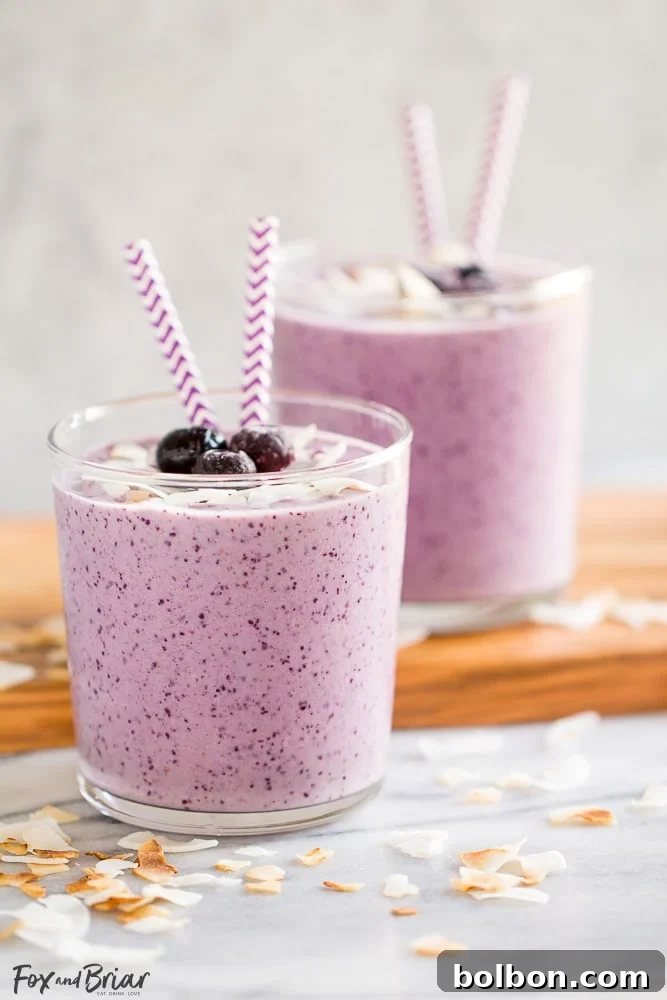 Close-up of a Blueberry Banana Coconut Smoothie in a glass, with a straw, showing its smooth texture and rich color.