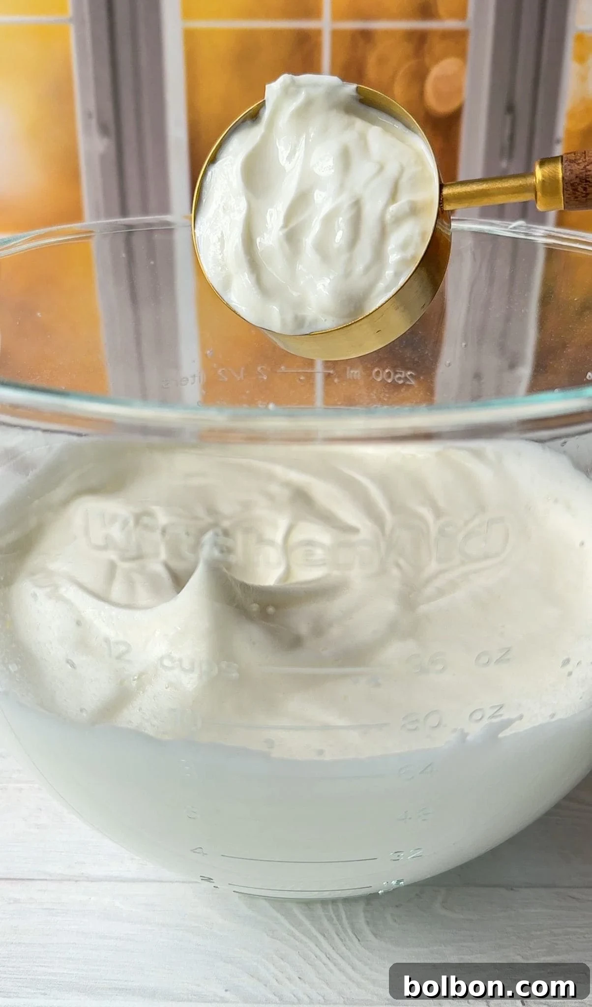 The Greek yogurt being carefully added to the bowl of whipped egg whites.