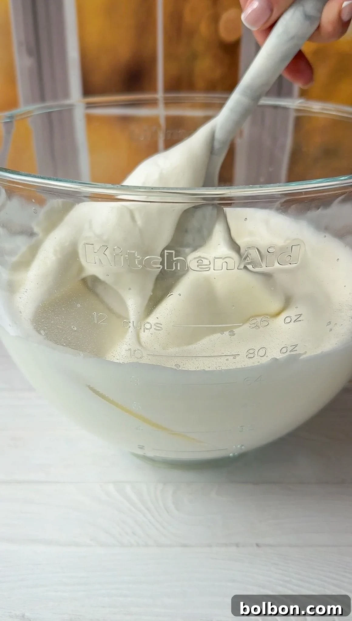 A spatula gently folding the Greek yogurt into the airy, fluffy egg whites mixture.