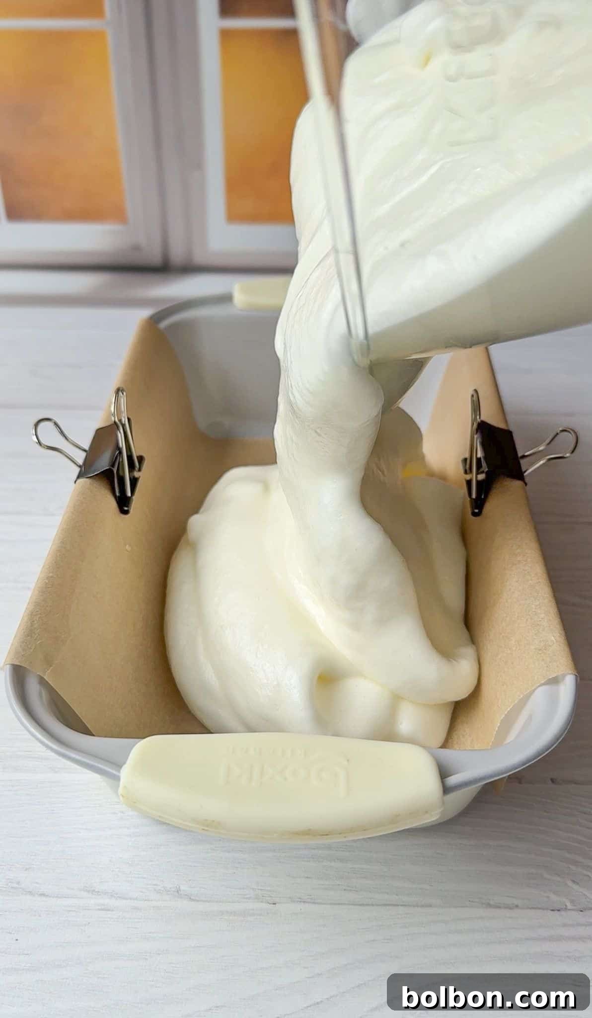 The Cloud Bread batter being poured smoothly into a parchment-lined bread pan, ready for baking.