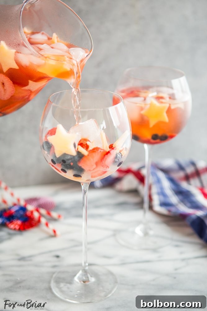 Kırmızı, Beyaz ve Mavi Şarap Punçları 4 A pitcher of Red, White, and Blue Wine Sparklers filled with fruit, ready to be served at a festive Fourth of July gathering.