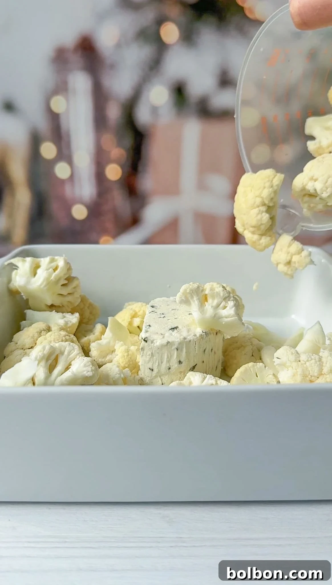A white baking dish filled with the florets and a block of cheese, with additional florets being poured in. 