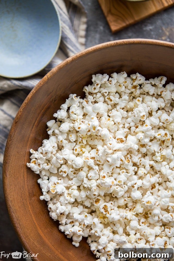 A rustic wooden spoon scattering truffle salt over a bowl of freshly made truffle popcorn. | best truffle salt | gourmet popcorn ingredients | cooking with truffles