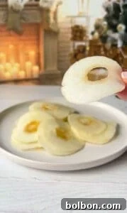 The Elusive Apple Cake 17 A hand holding a thinly sliced apple in front of a plate with more apple slices. In the background, there's a lit fireplace and a decorated Christmas tree.