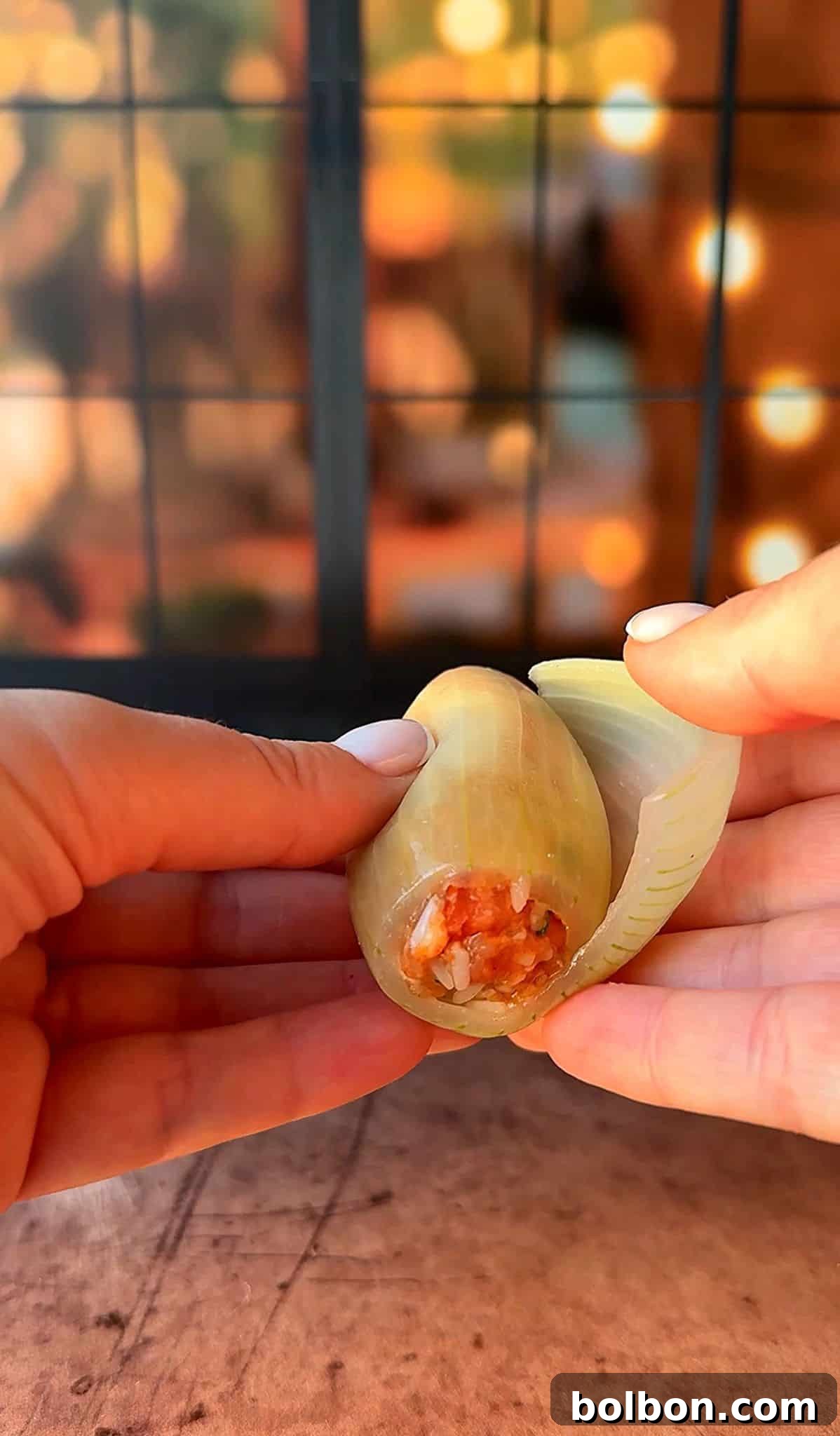 Golden Stuffed Onion Delights 13 Two hands are peeling open a large cooked shell to reveal a red and orange filling against a blurred background with warm lighting.