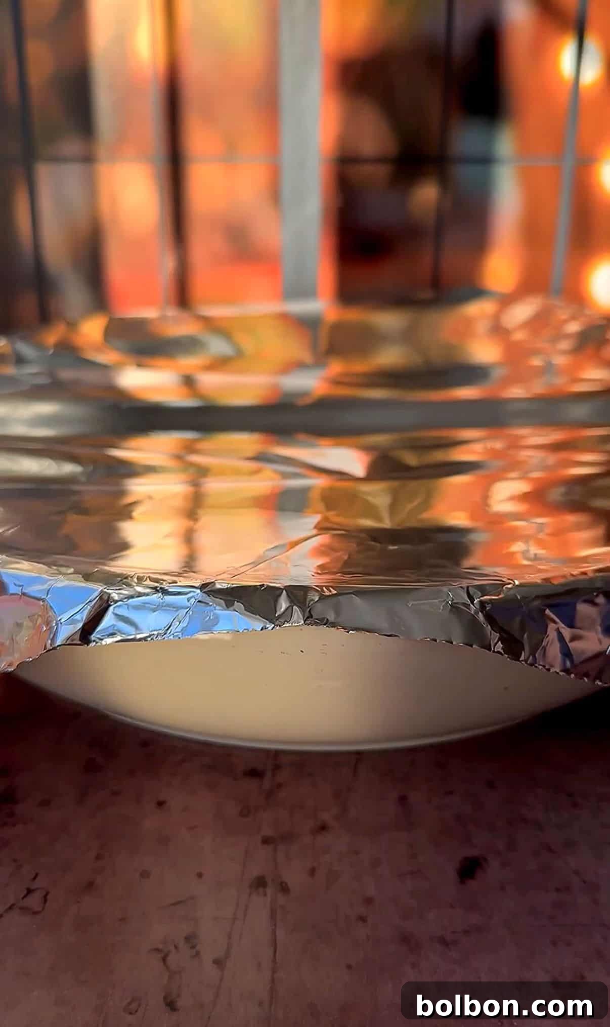 Golden Stuffed Onion Delights 16 A dish covered with aluminum foil sits on a surface. Warm, out-of-focus autumn colors are visible through a window in the background, creating a cozy atmosphere.