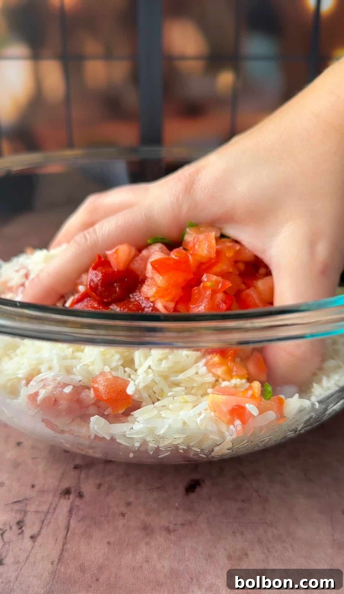 Golden Stuffed Onion Delights 5 A hand mixes white rice with diced tomatoes and green herbs in a clear glass bowl.