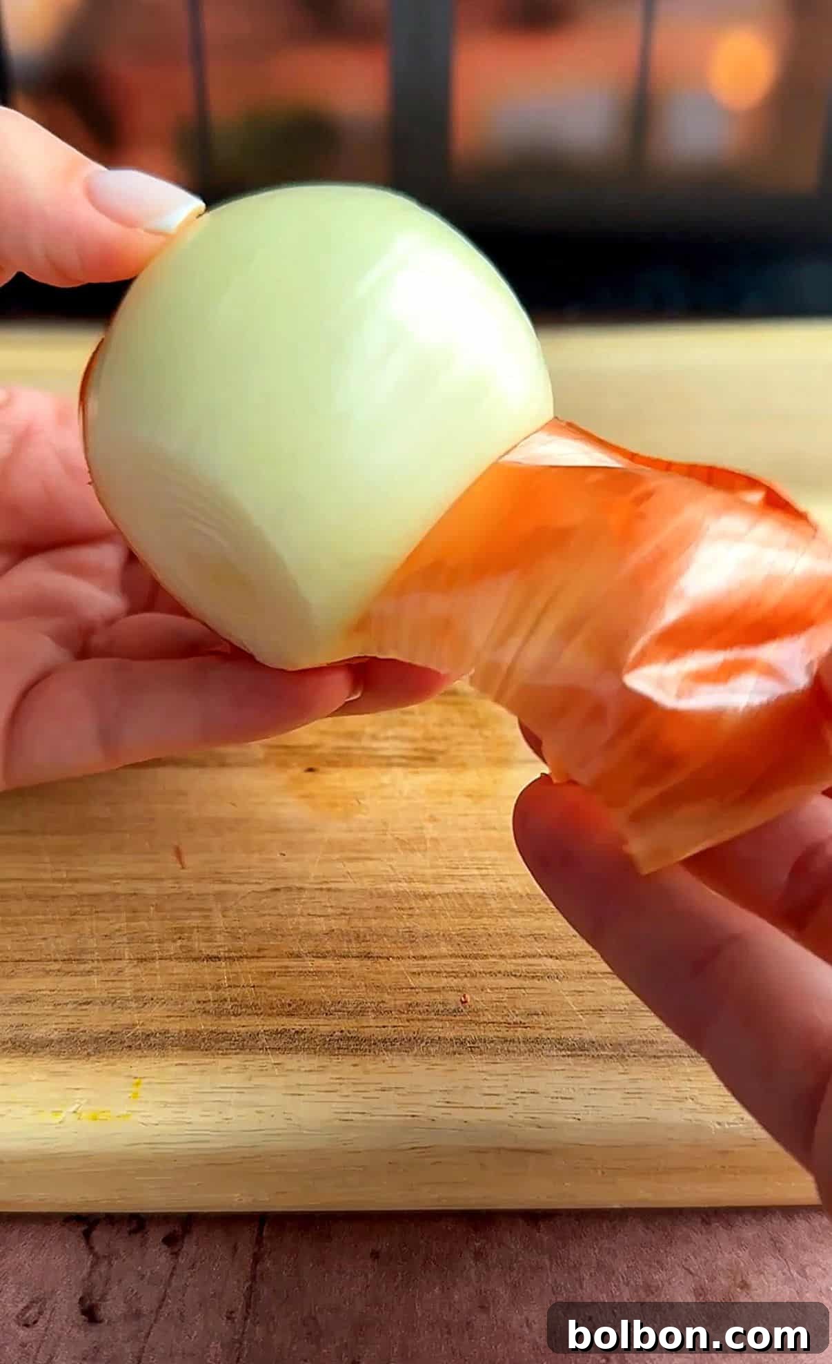 Golden Stuffed Onion Delights 6 A person peels the skin off a fresh onion over a wooden cutting board. The image focuses on the smooth, glossy surface of the onion, partially covered by papery brown skin.