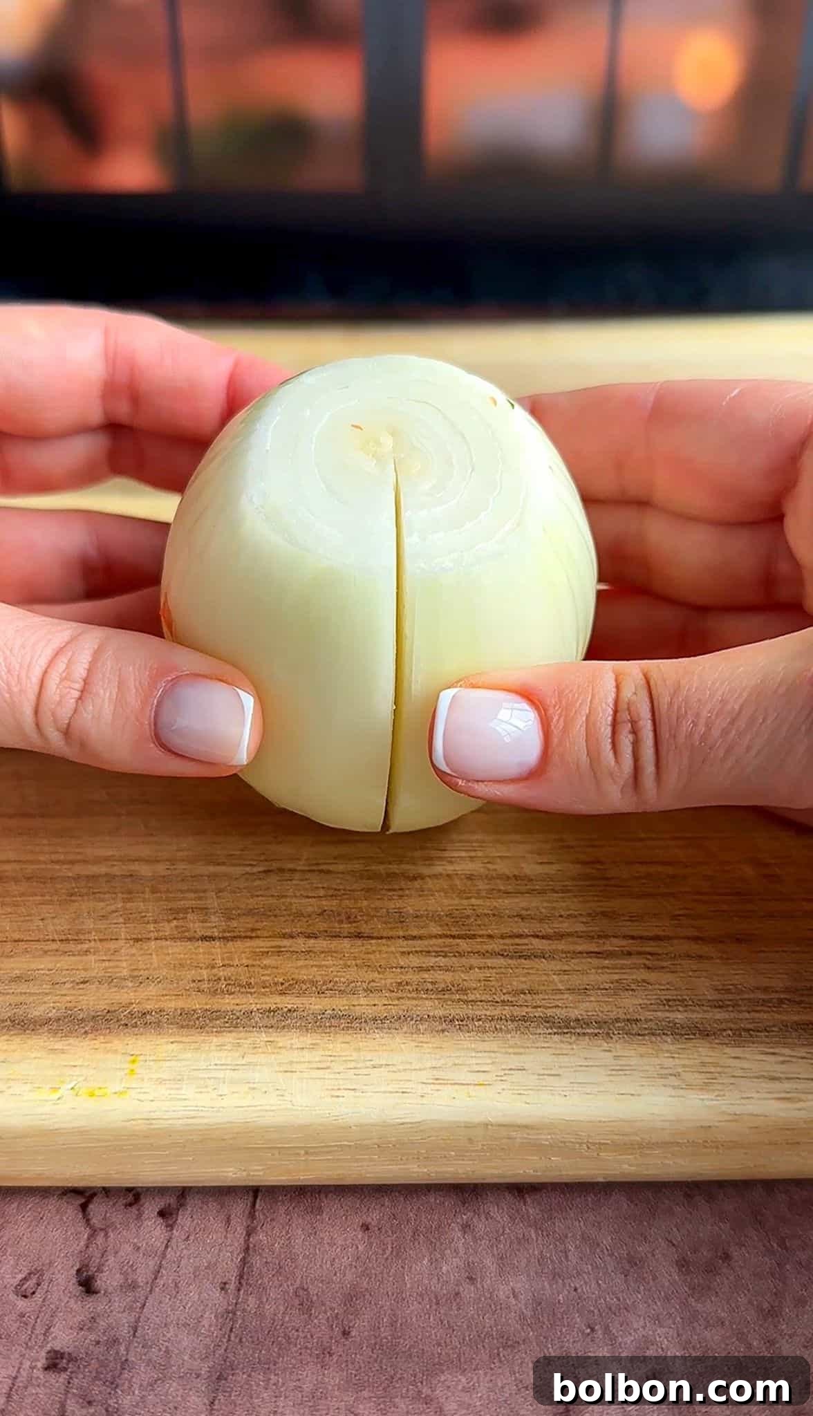 Golden Stuffed Onion Delights 8 Two hands holding a halved onion with the cut side facing the camera, placed on a wooden cutting board. The background is softly blurred.