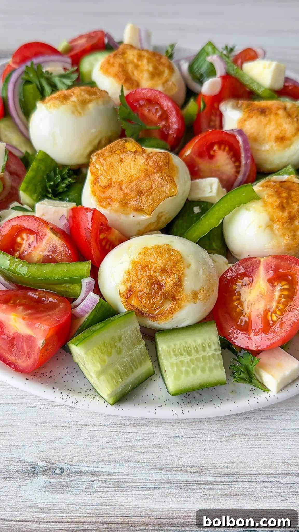 Crispy Golden Eggs 2 A vibrant salad featuring golden-crusted fried boiled eggs, colorful cherry tomatoes, refreshing cucumber slices, crisp green pepper, red onion, and fresh parsley, all beautifully arranged on a white plate. The eggs stand out with their unique crispy exterior amidst the fresh vegetables.