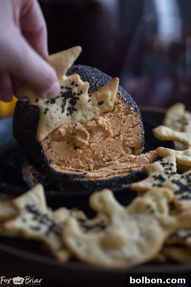 A perfectly round, orange cheese ball covered in dramatic black poppy seeds, presented elegantly on a dark platter, ideal for a classy Halloween party or adult gathering.