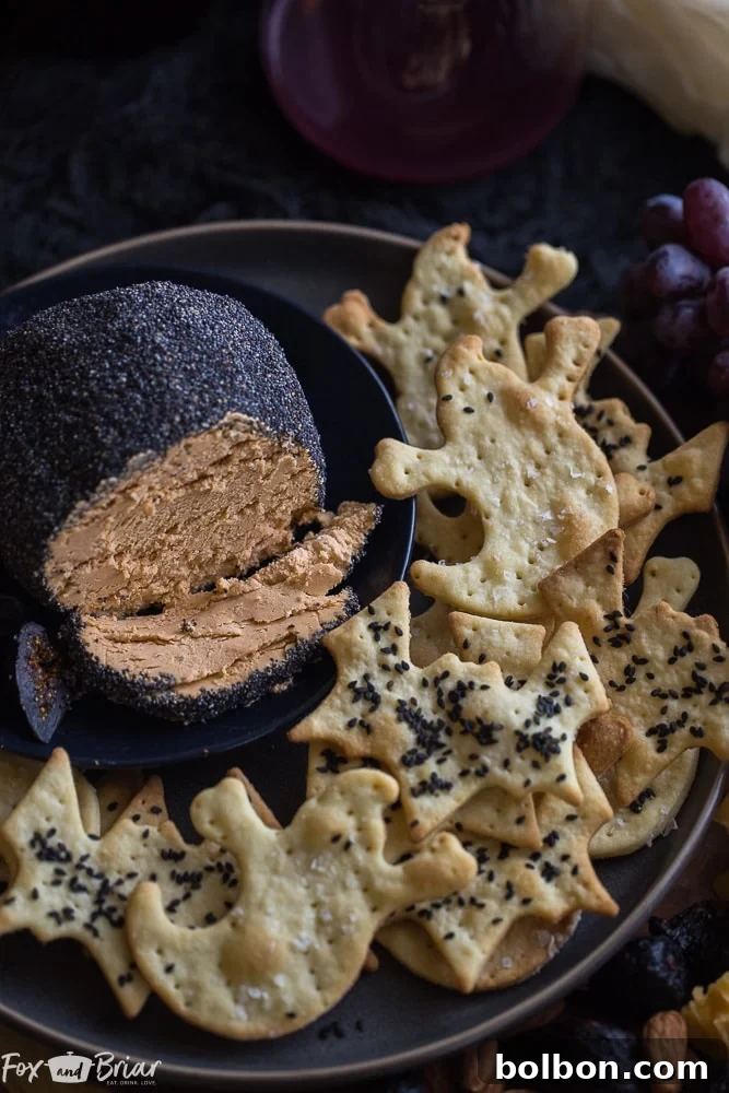 A high-angle view of the roasted garlic cheese ball, perfectly coated in black poppy seeds, presented elegantly on a serving board next to a small spreading knife and various crackers.