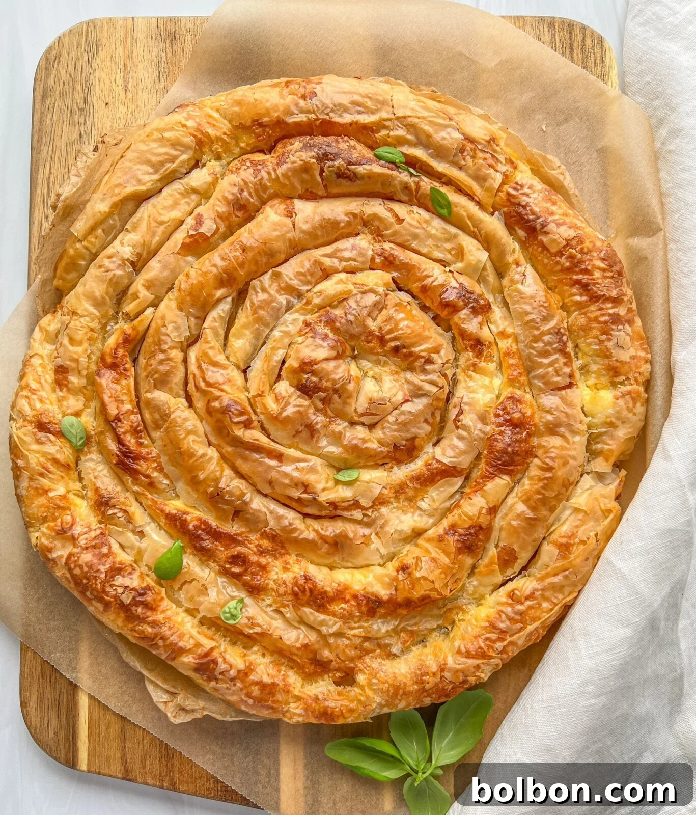A beautifully golden-brown, flaky Bulgarian Banitsa pie, spiraled and baked to perfection, sits on a wooden surface.