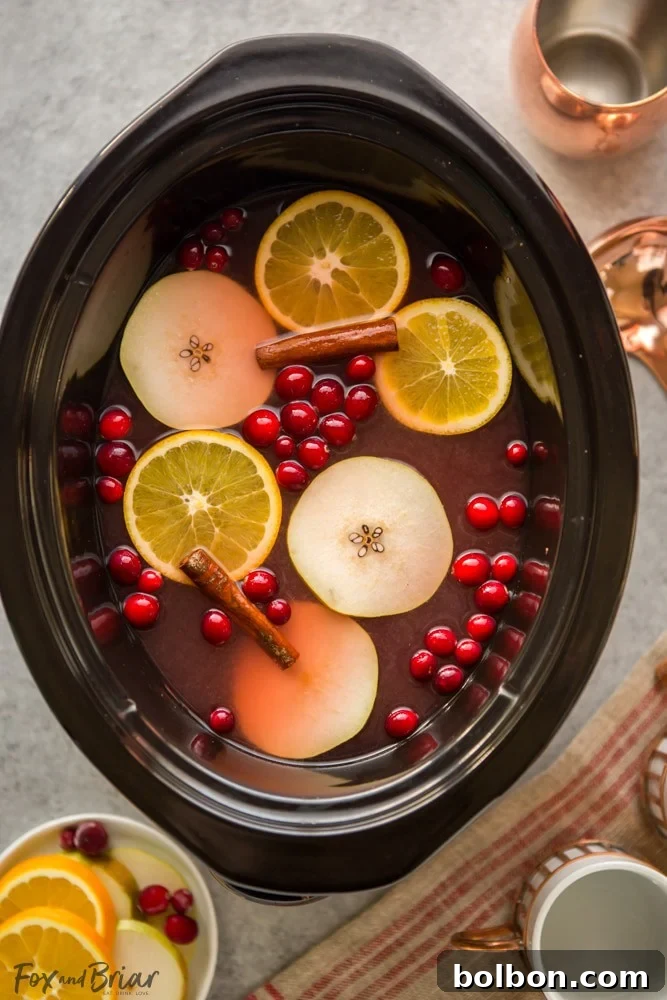Cozy mug of slow cooker cranberry pear cider, garnished with cranberries and orange slices, perfect for fall and winter holidays.