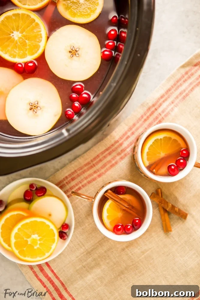 Overhead shot of slow cooker filled with pears, cranberries, orange, and spices, beginning to simmer.