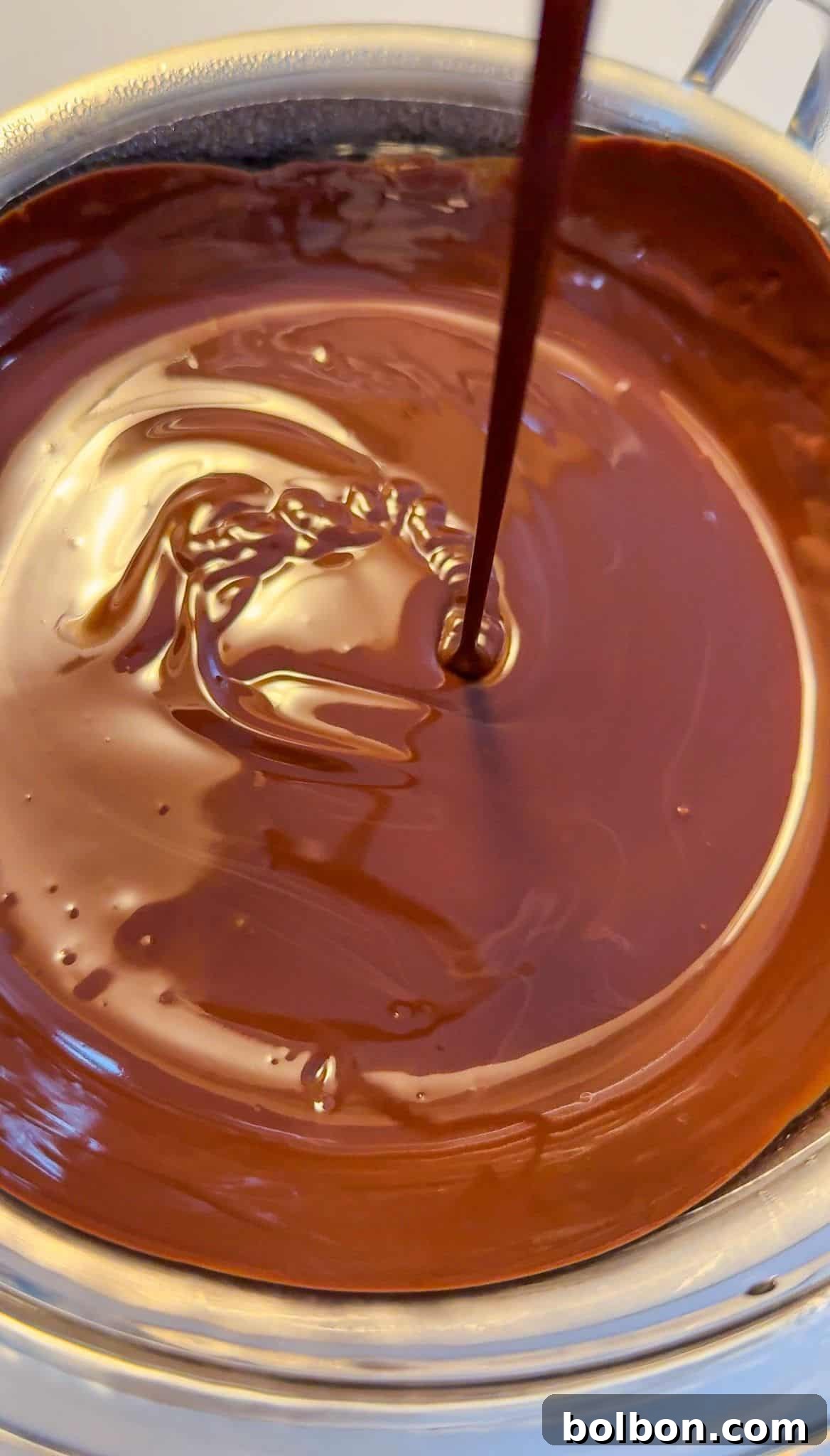 Exquisite Dubai Chocolate Dates 7 A stream of liquid chocolate pours into a bowl filled with melted chocolate, creating swirling patterns on the glossy surface.