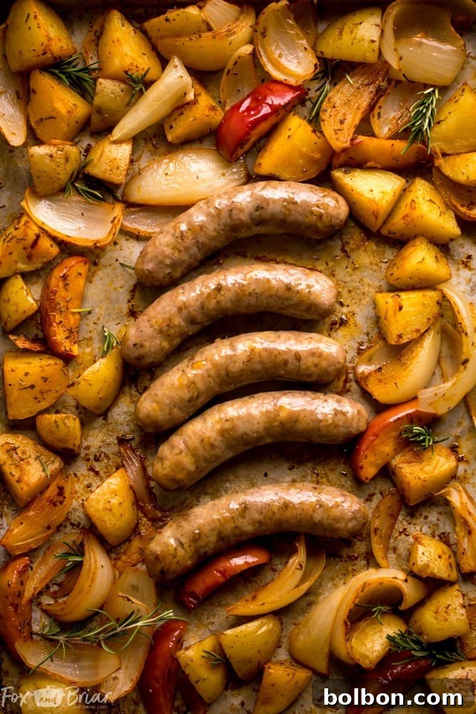 Close-up of roasted sausage, potatoes, onions, and apples on a baking sheet, showcasing a healthy sheet pan dinner.