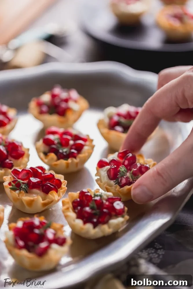 Close-up of Pomegranate Goat Cheese Bites, showcasing the creamy goat cheese, vibrant pomegranate arils, and fresh thyme, ready to serve at a party.
