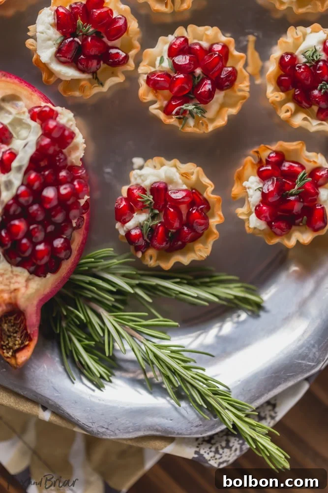 Pomegranate Goat Cheese Bites arranged on a wooden board, garnished with fresh thyme, perfect for a holiday party spread.
