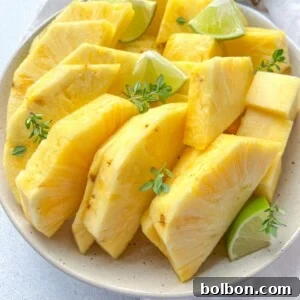A plate of fresh, sliced pineapple—showcasing how to cut pineapple—arranged with lime wedges and garnished with small green herbs on a light-colored surface.